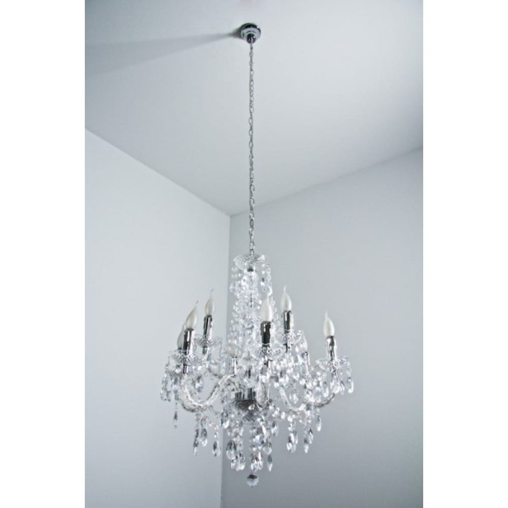 Luster żyrandol 9-punktowy, transparentny, z metalowymi detalami w kolorze chromu. Posiada dziewięć źródeł światła w formie świeczek, zawieszony na łańcuchu. Widoczny w aranżacji na jasnym tle, podkreślający elegancję wnętrza.