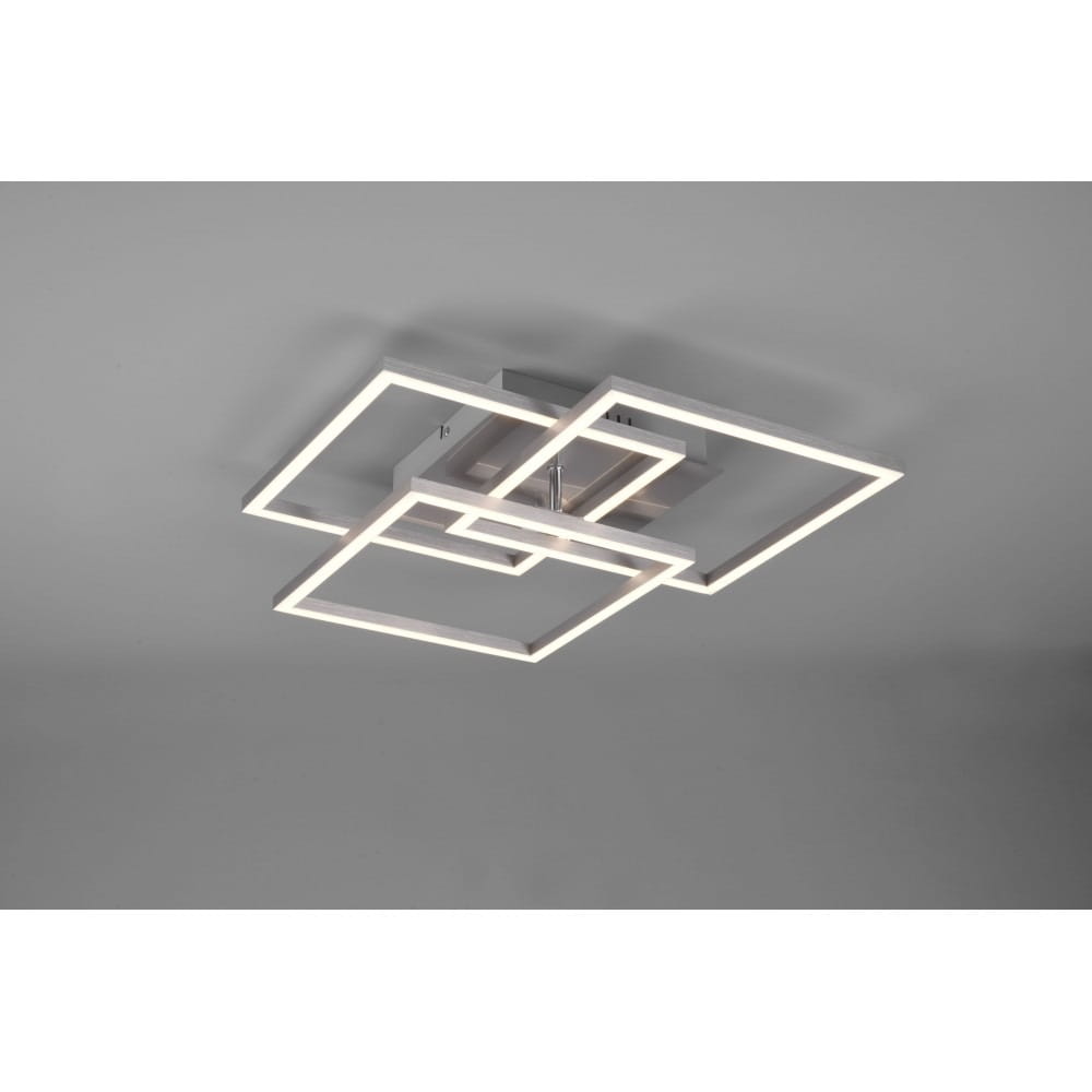 Trójpunktowa lampa sufitowa LED w kolorze niklowym, składająca się z nałożonych na siebie prostokątów, z ciepłym światłem. Ujęcie z góry, zamontowana na suficie, z pilotem do zdalnego sterowania.
