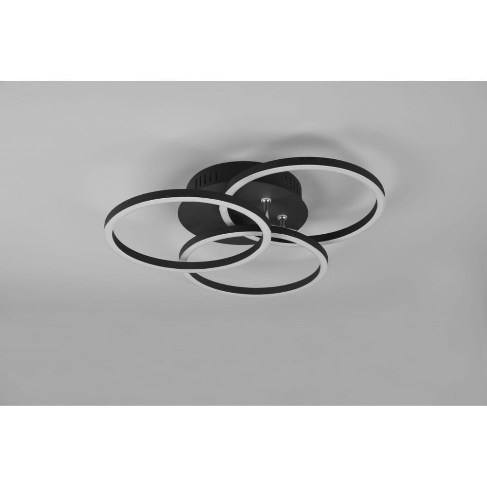 Czarna lampa sufitowa LED 3-punktowa z pilotem, z trzema okrągłymi pierścieniami w białym kolorze. Ujęcie z dołu, ukazujące unikalny design oraz mocowanie do sufitu. Prosta aranżacja na jasnym tle.