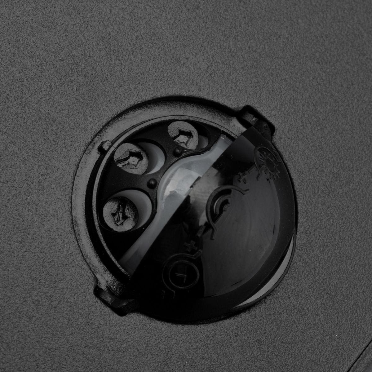 Czarny kinkiet elewacyjny Clark LED z czujnikiem ruchu, widok z bliska na okrągłą obudowę czujnika. Widać trzy śruby mocujące oraz oznaczenia funkcji na obudowie. Produkt ma matową powierzchnię grafitową.