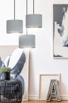 Lampa wisząca Hilde 3-punktowa w kolorze szarym z okrągłymi kloszami, zawieszona na czarnych linkach. Klosze mają matową fakturę, a ich wnętrze jest jasne, co zapewnia efektowne oświetlenie. W tle widoczna dekoracja ścienna oraz roślinność.