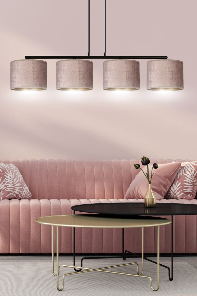 Lampa wisząca Hilde 4-punktowa w kolorze różowym, z czterema okrągłymi kloszami z tkaniny, zamocowana na czarnym stelażu. Ujęcie frontalne, lampa zawieszona nad czarnym stolikiem, w tle różowa kanapa z ozdobnymi poduszkami.