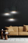 Czarna lampa wisząca Hilde 3-punktowa z cylindrycznymi kloszami, zawieszona na cienkich linkach. Klosze mają złote wnętrze, emitujące jasne światło. Lampa umieszczona nad brązową sofą w nowoczesnym wnętrzu z ciemnym tłem.