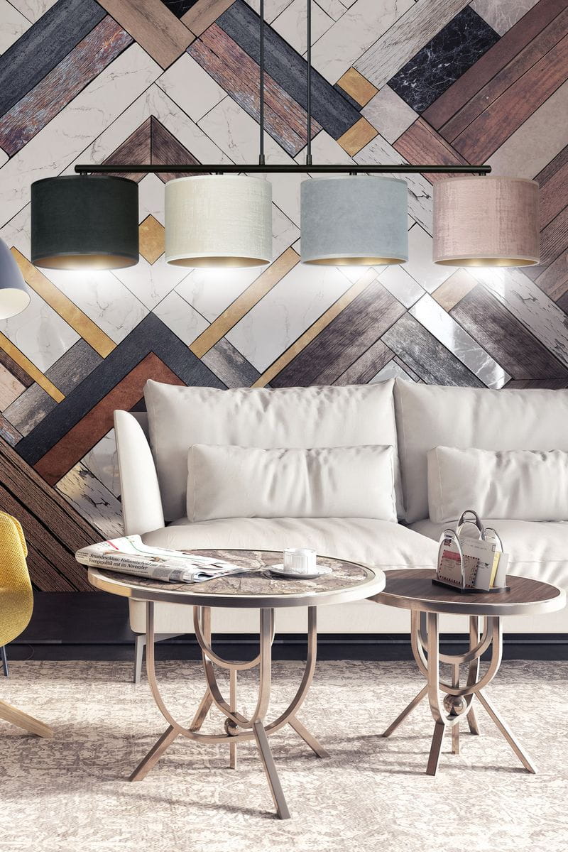 Lampa wisząca Hilde 4-punktowa w multikolorze, z czterema cylindrycznymi kloszami w różnych kolorach (ciemna zieleń, jasny beż, błękitny, różowy), zawieszona na czarnym stelażu, w nowoczesnym wnętrzu z sofą i okrągłymi stolikami.