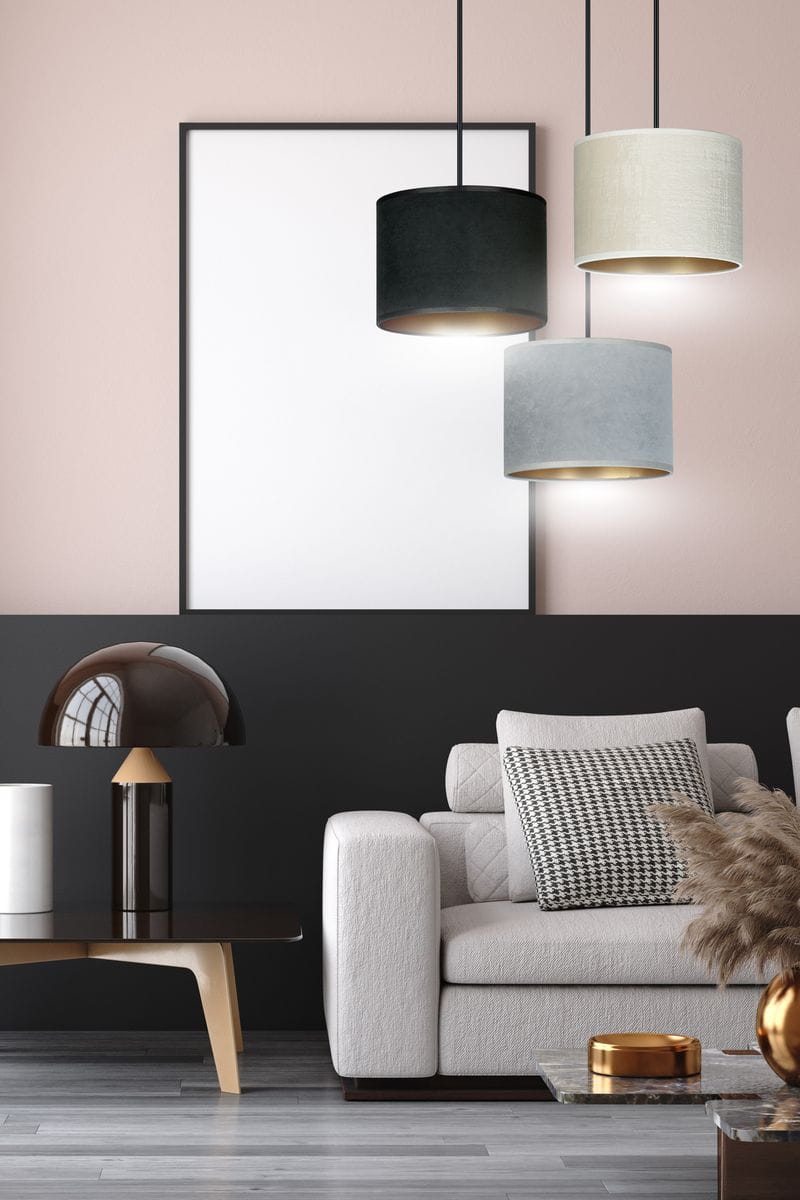 Lampa wisząca Hilde 3-punktowa w kolorach czarnym, szarym i kremowym, z okrągłymi kloszami wykonanymi z materiału, zawieszona na cienkich linkach. W tle minimalistyczna aranżacja salonu z jasną sofą i ciemną ścianą.