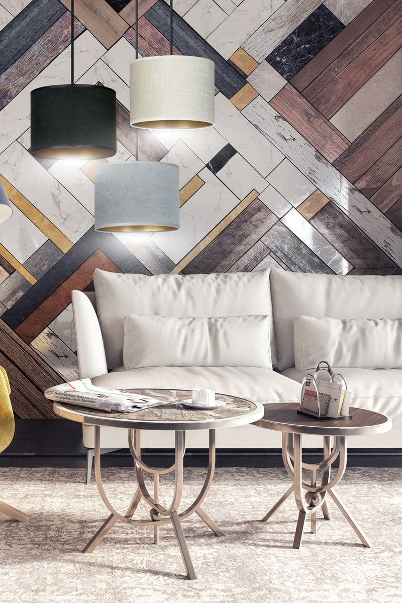 Lampa wisząca Hilde 3-punktowa w kolorach multikolorowych, z okrągłymi abażurami w odcieniach czerni, beżu, szarości i błękitu. Zawieszona na czarnych przewodach, umiejscowiona nad stolikami kawowymi w nowoczesnym wnętrzu z jasną kanapą.