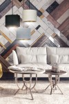 Lampa wisząca Hilde 3-punktowa w kolorach multikolorowych, z okrągłymi abażurami w odcieniach czerni, beżu, szarości i błękitu. Zawieszona na czarnych przewodach, umiejscowiona nad stolikami kawowymi w nowoczesnym wnętrzu z jasną kanapą.