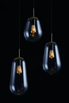 Lampa wisząca Pear w konfiguracji 3-punktowej z trzema szklanymi kloszami w kształcie kropli, w kolorze przezroczystym, z widocznymi żarówkami. Metalowe elementy w kolorze złotym. Produkt zawieszony na cienkich linkach, na jednolitym, ciemnym tle.