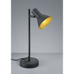 Czarna lampa stołowa Nina z jednopunktowym źródłem światła. Okrągła, matowa podstawa, smukły metalowy stelaż i klosz w kształcie stożka z wewnętrzną złotą powłoką. Ujęcie z boku, na jednolitym tle.