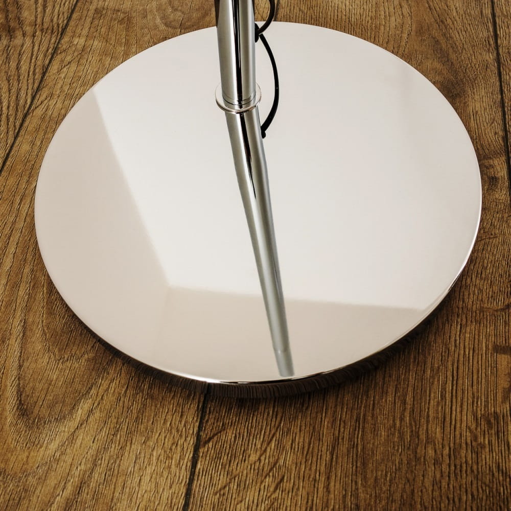 Lampa podłogowa Brasilia z chromowanym stelażem, widok z dołu. Okrągła, lustrzana podstawa odbijająca światło, z cienką, prostą nogą. Tło to drewniana podłoga w ciepłym odcieniu.
