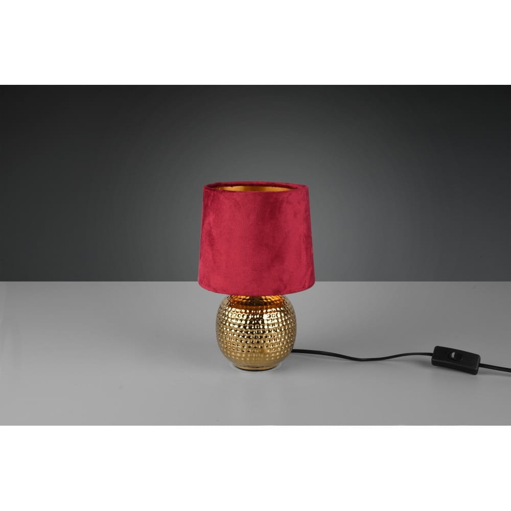 Czerwona lampa stołowa Sophia z 1 punktem świetlnym, z okrągłym, złotym korpusem o teksturowanej powierzchni. Abajur z czerwonego, aksamitnego materiału, z wnętrzem w kolorze złotym. Zasilanie z przewodem z włącznikiem.