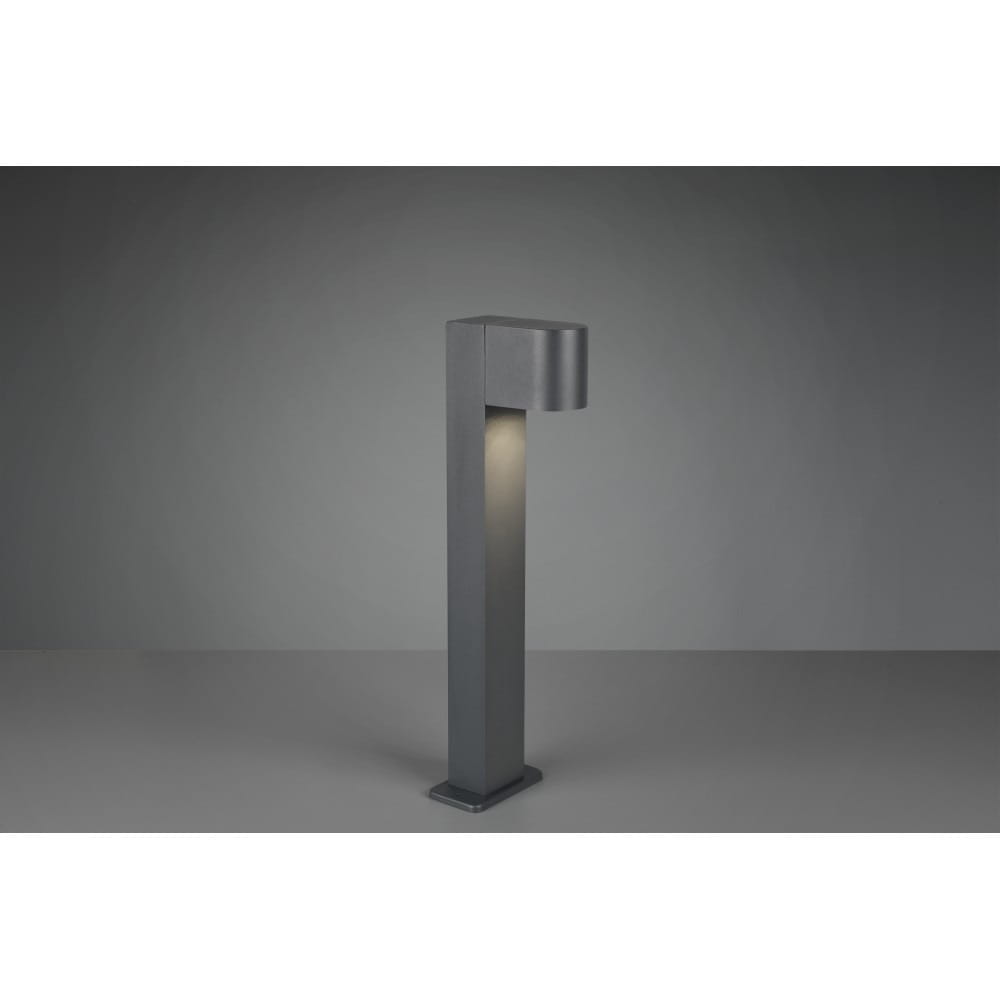 Lampa stojąca ogrodowa Roya H50 w kolorze antracytowym, o kwadratowej podstawie i prostokątnym korpusie. Ujęcie z boku, z widocznym kloszem na górze, emitującym światło. Tło jednolite, szare.