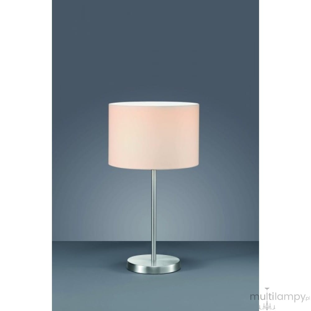 Lampa stołowa 1-punktowa w kolorze białym z okrągłym kloszem, na metalowej podstawie. Ujęcie frontalne, lampa stoi na płaskiej powierzchni, z jednolitym tłem w odcieniu szaro-niebieskim.