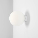 Biały kinkiet Ball D14 z pojedynczym punktem świetlnym, z kulistym kloszem w matowym wykończeniu. Montowany na ścianie, zamocowany na okrągłej podstawie. Tło jasne, jednolite.
