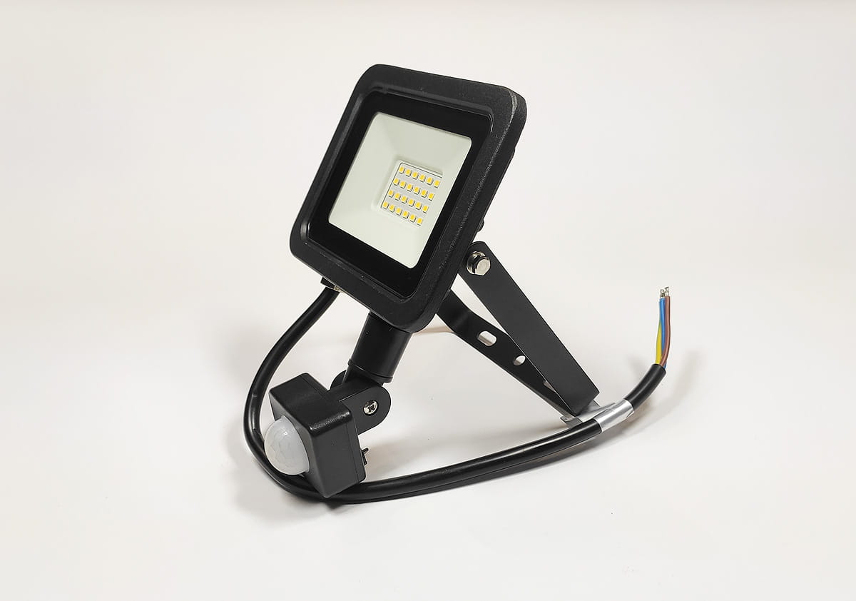 Naświetlacz LED halogenowy 20W z czujnikiem ruchu, kolor czarny. Kwadratowa głowica z wieloma diodami LED, umieszczona na regulowanym ramieniu. Widoczny kabel podłączający oraz czujnik ruchu w dolnej części. Wodoodporność IP65.
