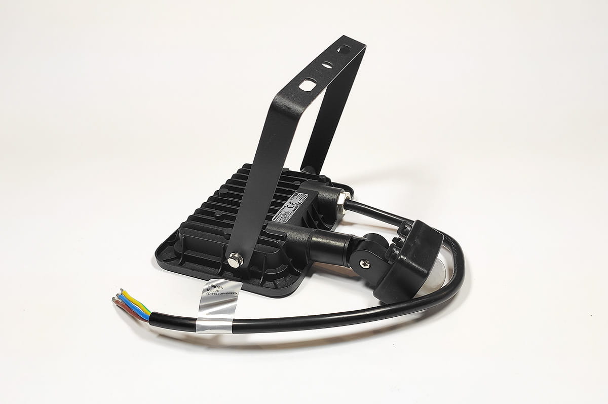 Naświetlacz LED halogen 20W z czujnikiem ruchu, o temperaturze barwowej białej zimnej. W czarnej obudowie z radiatorami, zamontowany na regulowanym uchwycie. Widoczne przewody elektryczne w kolorze żółto-zielonym, niebieskim i brązowym.