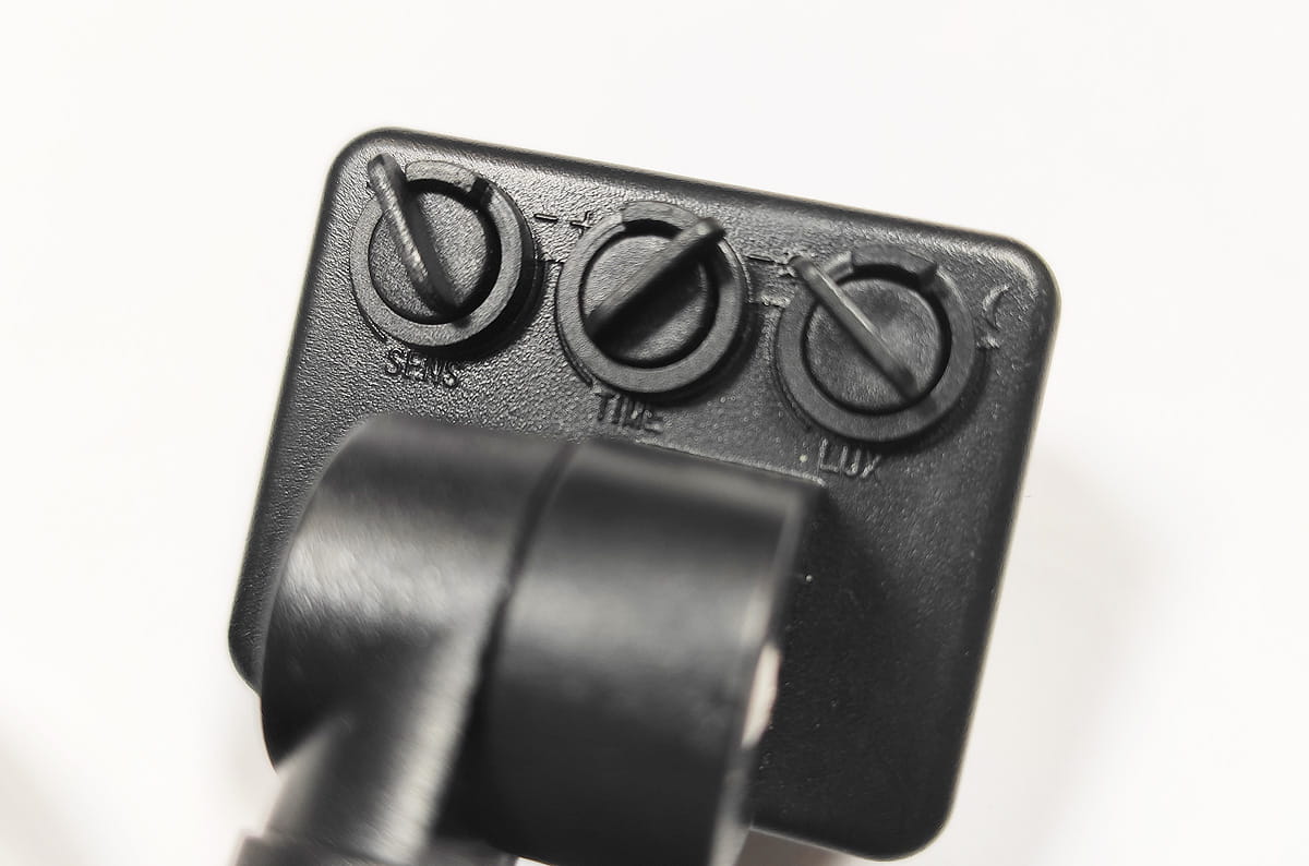 Czarny naświetlacz LED halogen z czujnikiem ruchu, widoczny z bliska. Na tylnej stronie znajdują się trzy regulacyjne pokrętła oznaczone SENS, TIME i LUX. Produkt ma metalową konstrukcję, przeznaczoną do montażu na zewnątrz, w klasie ochrony IP65.
