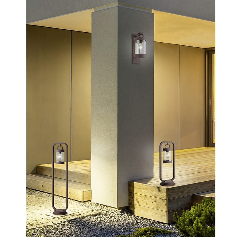 Lampa ogrodowa stojąca Sambesi H100 w kolorze antracytowym z czujnikiem zmierzchu, o cylindrycznym kształcie, umieszczona na podłodze. W tle widoczny element architektoniczny i drewniana podłoga.