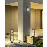 Lampa ogrodowa stojąca Sambesi H100 w kolorze antracytowym z czujnikiem zmierzchu, o cylindrycznym kształcie, umieszczona na podłodze. W tle widoczny element architektoniczny i drewniana podłoga.