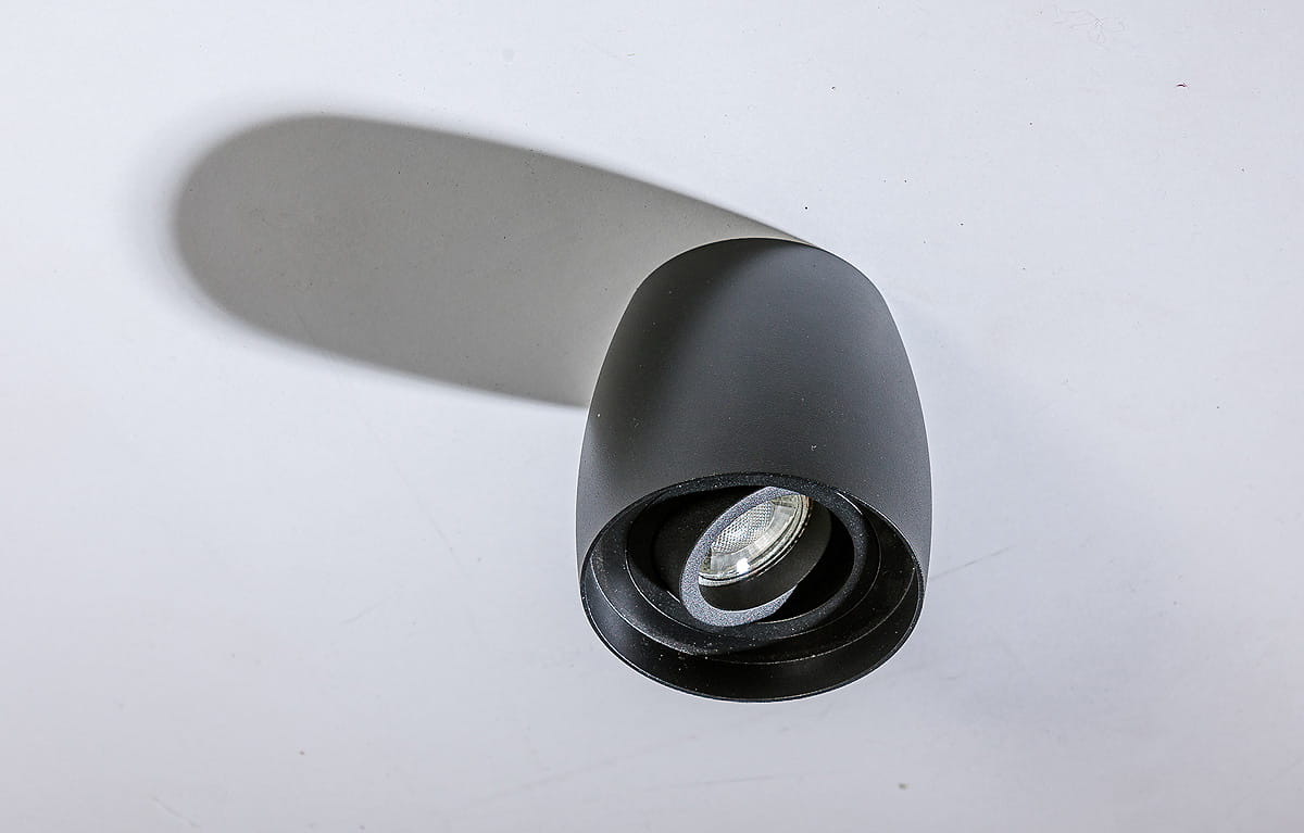 Czarna lampa sufitowa kierunkowa Rotondo AZ4208, o opływowym kształcie, z widoczną żarówką w centralnej części. Ujęcie z góry, na białym tle, ukazujące detale konstrukcji i fakturę matowego wykończenia.