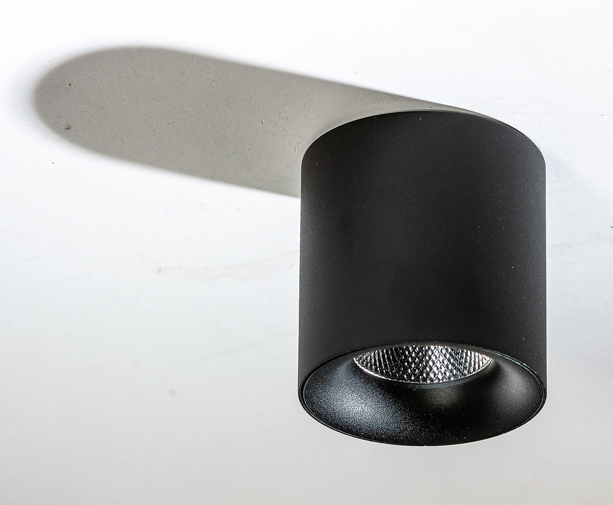 Mane LED lampa sufitowa 1-punktowa 10W/4000K w kolorze czarnym, o cylindrycznym kształcie, montowana na suficie. Wnętrze lampy z siatkowym wykończeniem, rzucająca cień na powierzchnię.