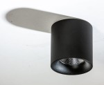 Czarna lampa sufitowa LED 1-punktowa z metalową obudową, o okrągłym kształcie. Widoczny klosz z teksturowanym wnętrzem, emitujący ciepłe światło 3000K. Ujęcie z dołu, widać cień na powierzchni podłogi.