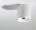 Biała lampa sufitowa LED 1-punktowa o mocy 10W i barwie światła 3000K, w kształcie cylindrycznym. Zamontowana na suficie, z widoczną, metalową osłoną żarówki. Kąt ujęcia z góry, na jednolitym tle.