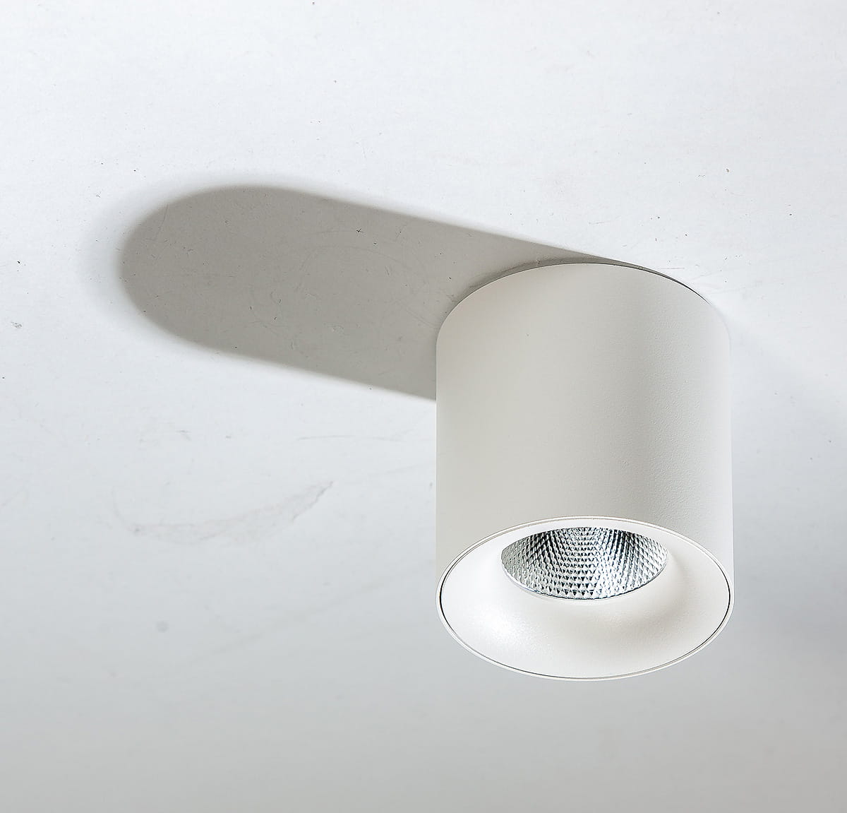 Biała lampa sufitowa LED 1-punktowa o mocy 10W i temperaturze barwowej 4000K, okrągła z metalowym wykończeniem. Widoczna struktura klosza, zamontowana na gładkim, jasnym suficie, rzucająca cień na powierzchnię.