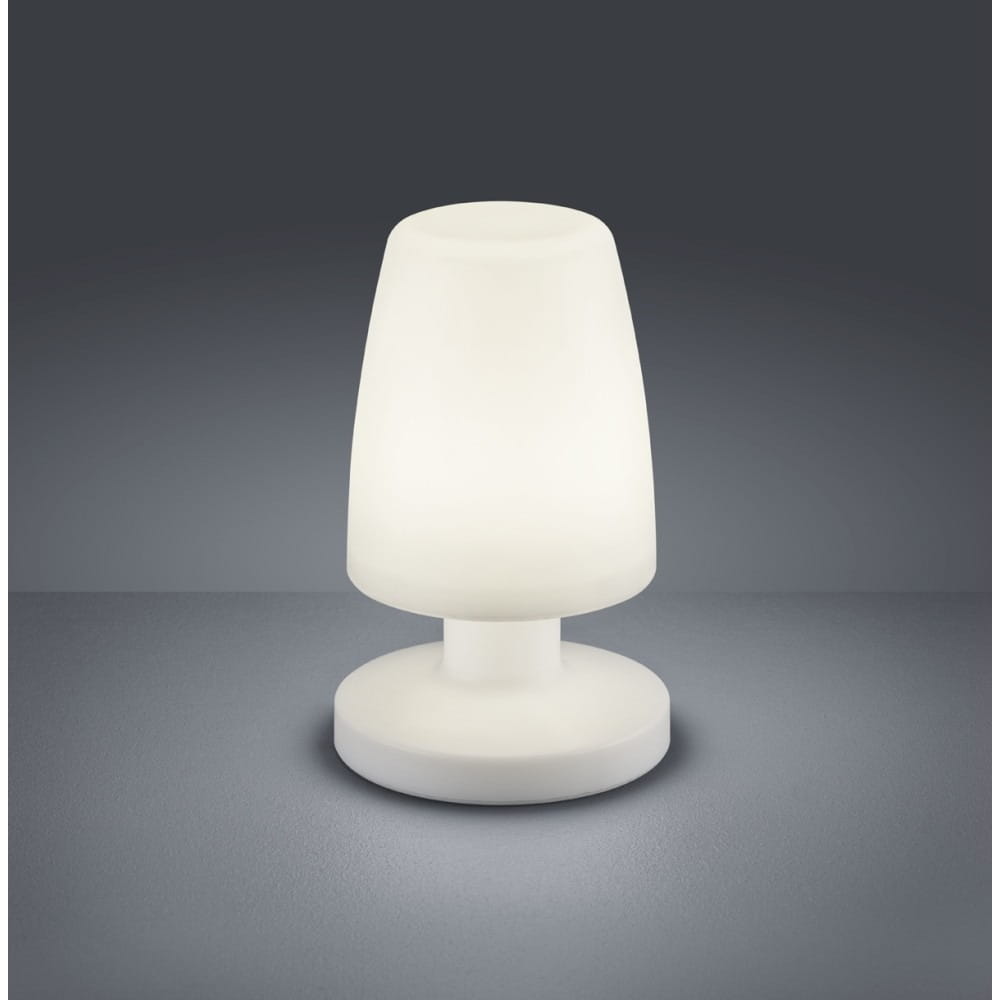 Biała lampa stołowa Dora LED o zaokrąglonym kształcie, umieszczona na okrągłej podstawie. Wykonana z matowego materiału, emituje miękkie światło. Ujęcie z przodu, na jednolitym ciemnym tle. Idealna do użytku w ogrodzie lub na tarasie.