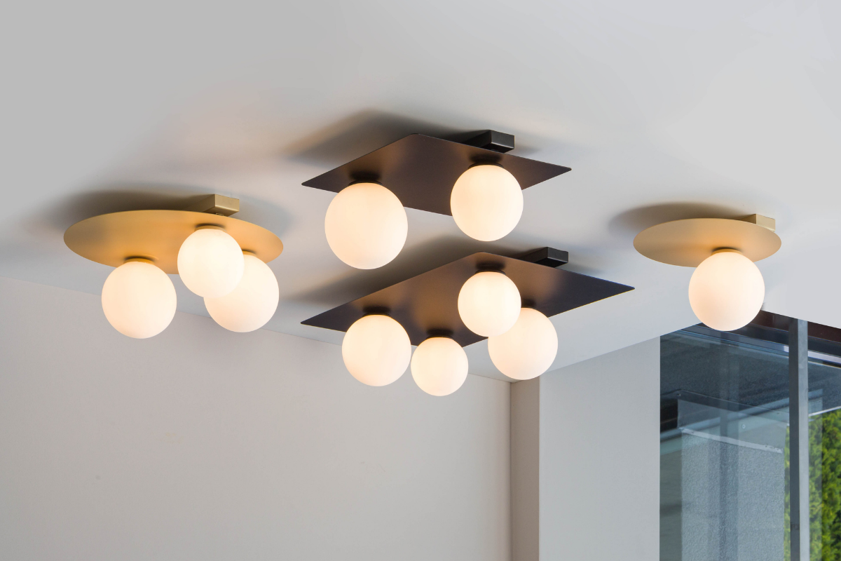 Okrągła lampa sufitowa Argon w kolorze złotym z trzema punktami świetlnymi. Każda oprawa ma mleczne, okrągłe klosze. Lampa zamontowana na suficie, w nowoczesnym wnętrzu, z widocznym podziałem na elementy w różnych kształtach.