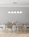 Lampa wisząca Ramon 5-punktowa w wykończeniu chromowym. Zawieszona na cienkich kablach, z pięcioma okrągłymi kloszami w białym kolorze. Umieszczona nad drewnianym stołem w nowoczesnej jadalni, z szarymi krzesłami i minimalistycznymi dekoracjami.