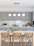 Lampa wisząca Ramon 4-punktowa w chromowanym wykończeniu z czterema okrągłymi, białymi kloszami, zawieszona nad białym stołem w nowoczesnej kuchni z szarymi szafkami i drewnianymi krzesłami.