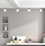 Lampa sufitowa Oden 1-punktowa w chromowanym wykończeniu, z okrągłą, białą żarówką. Ujęcie z przodu, zamontowana na suficie w minimalistycznym wnętrzu, obok dekoracyjnych elementów na półce. Tło w jasnym kolorze.