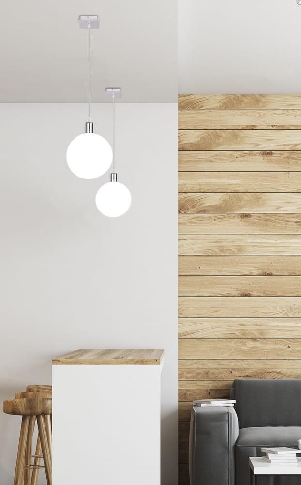 Lampa wisząca Oden D15 w chromowanej oprawie, z dużą, białą kulą szklana. Zawieszona na cienkim przewodzie, w nowoczesnym wnętrzu z drewnianą ścianą i jasnym blatem. Idealna do oświetlenia przestrzeni.