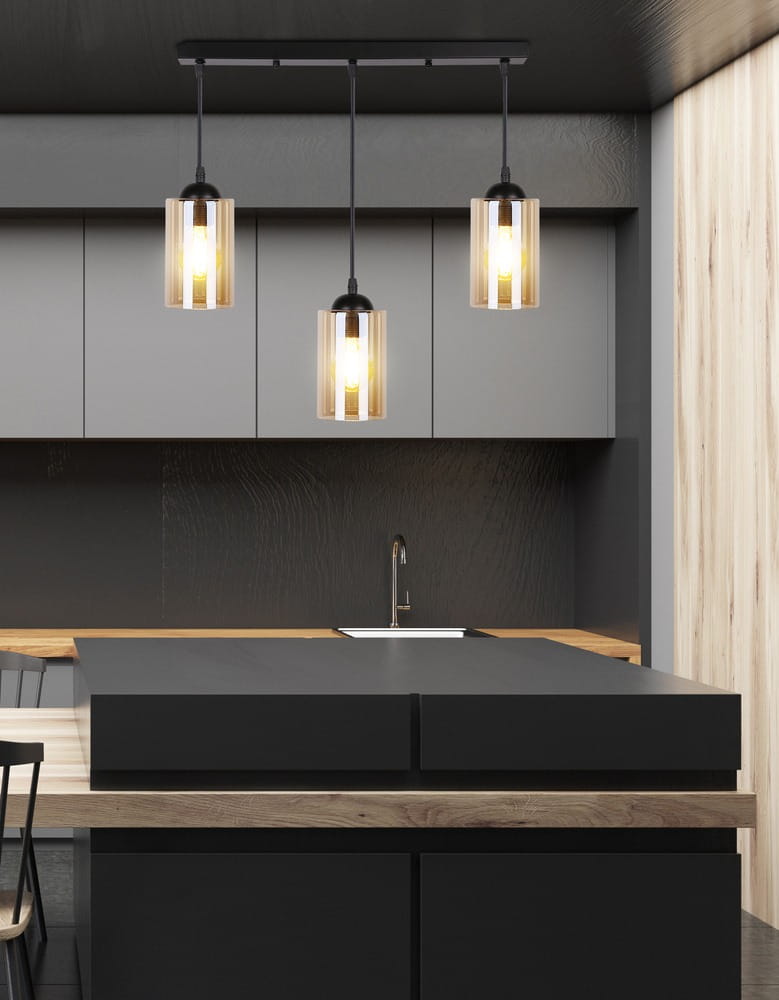 Czarna lampa wisząca 3-punktowa Bistro z przezroczystymi kloszami, zawieszona na prostej, czarnej listwie. Klosze mają cylindryczny kształt, emitując ciepłe światło. Lampa umieszczona nad czarnym blatem kuchennym w nowoczesnym wnętrzu.
