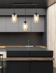 Czarna lampa wisząca 3-punktowa Bistro z przezroczystymi kloszami, zawieszona na prostej, czarnej listwie. Klosze mają cylindryczny kształt, emitując ciepłe światło. Lampa umieszczona nad czarnym blatem kuchennym w nowoczesnym wnętrzu.