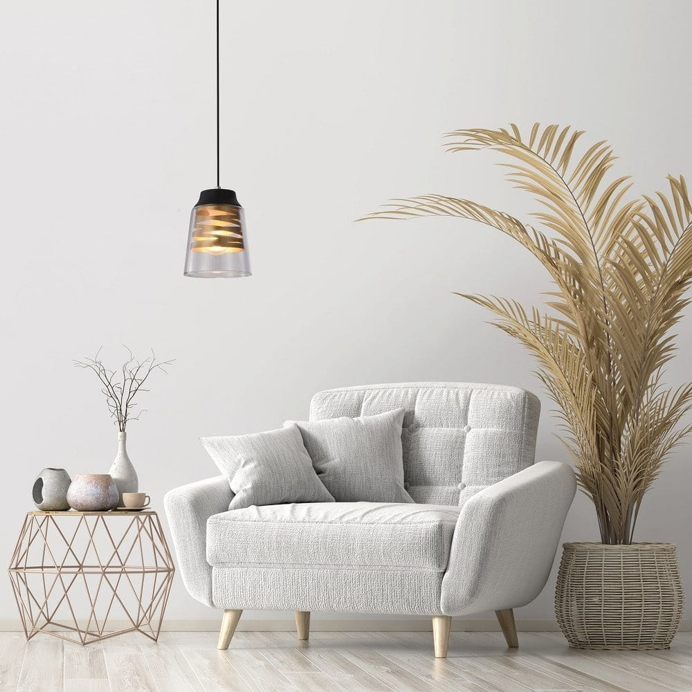 Czarna lampa wisząca Fresno 1-punktowa z przezroczystym kloszem, zawieszona nad jasną sofą. W tle widoczna palma oraz dekoracyjny stół z wazonami i filiżankami. Minimalistyczne wnętrze w neutralnych kolorach.