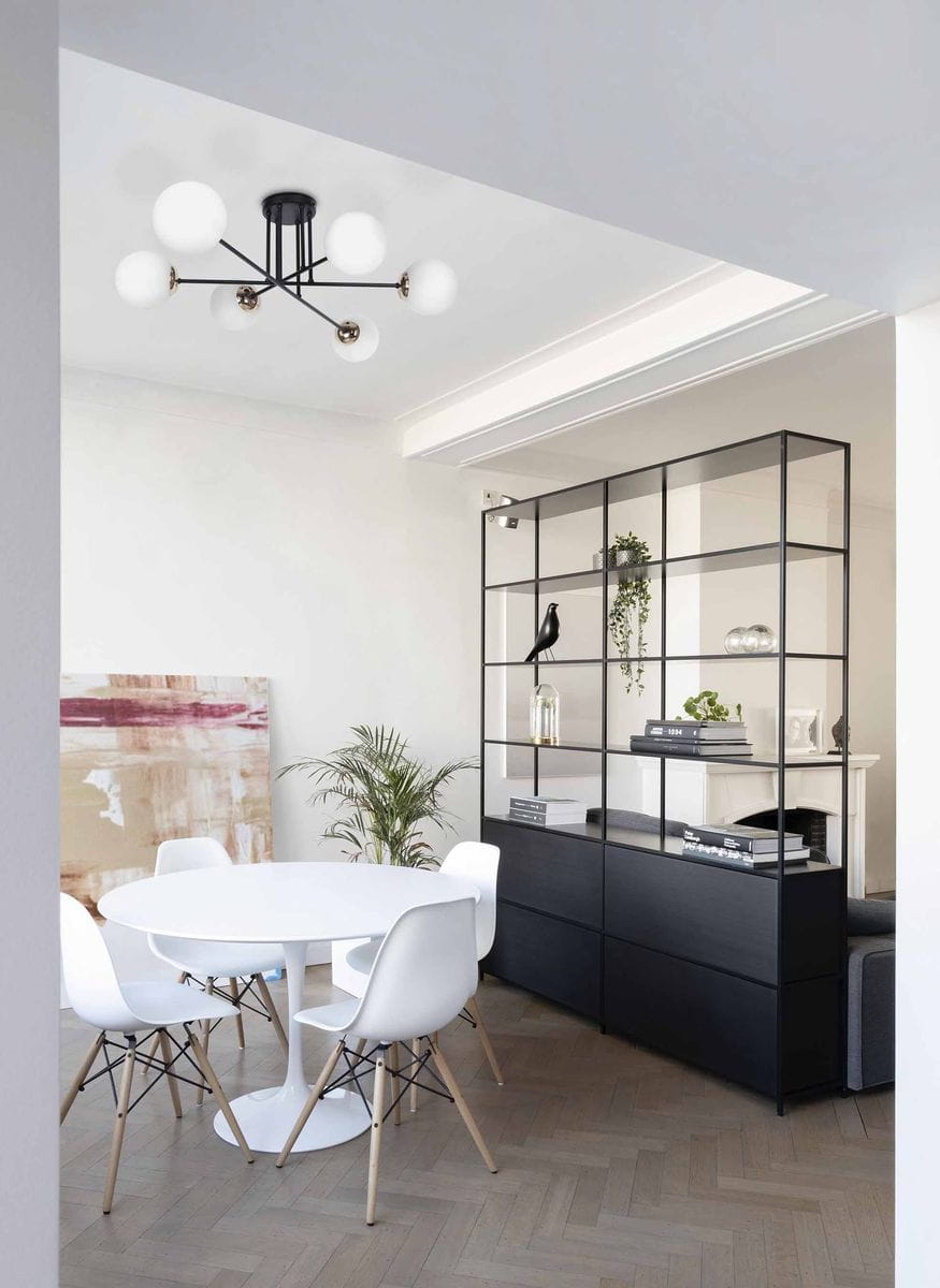 Lampa sufitowa Isla, 6-punktowa, w kolorze czarnym z elementami w patynie. Ułożona na suficie, z sześcioma białymi kloszami w kształcie kul, otaczającymi centralny uchwyt. W tle widoczne nowoczesne wnętrze z białym stołem i krzesłami.
