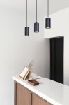 Czarna lampa wisząca Puerto K-4895 o cylindrycznym kształcie, zawieszona na długim kablu, z widocznym złotym wnętrzem. Umieszczona w minimalistycznym wnętrzu z białym blatem i drewnianymi akcentami.