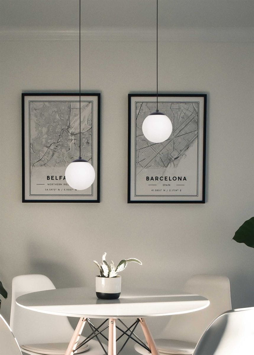 Lampa wisząca Savoy D16 w kolorze czarnym, z okrągłym kloszem w białym kolorze, zawieszona na cienkim przewodzie. Ujęcie frontalne, lampa w nowoczesnym wnętrzu z mapami w ramkach na ścianie oraz okrągłym stołem i rośliną.