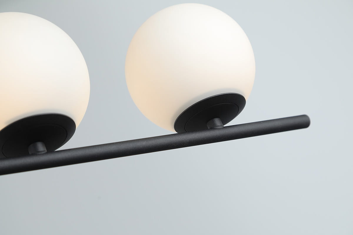 Czarna lampa wisząca Santander z czterema punktami świetlnymi. Okrągłe klosze w opalowym kolorze, umieszczone na poziomej, matowej rurze. Ujęcie z góry, pokazujące szczegóły mocowania i kształt kloszy.