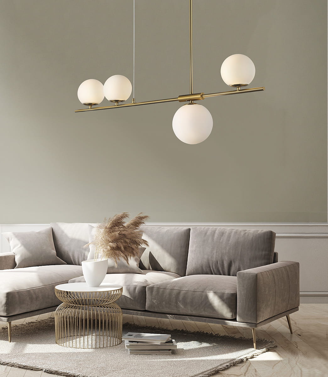Lampa wisząca Santander 4-punktowa w kolorze złotym, z trzema szklanymi kulami o białej barwie, zawieszona na cienkim, prostym stelażu. Produkt umieszczony nad sofą w nowoczesnym wnętrzu, na tle jasnej ściany.