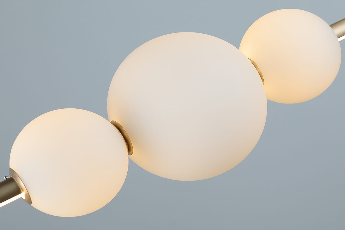 Lampa wisząca Sandra LED 1-punktowa w kolorze złotym z trzema matowymi, okrągłymi kloszami. Klosze są umieszczone na złotym stelażu, tworząc nowoczesny design. Ujęcie z bliska, skupiające się na detalach kloszy i mocowania.