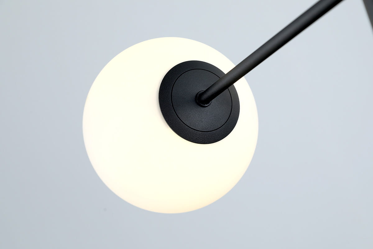 Lampa wisząca Oviedo 6-punktowa w kolorze czarnym. Okrągła, matowa kula z białym kloszem, zawieszona na cienkim, czarnym ramieniu. Widok z dołu, ukazujący detal mocowania do sufitu oraz elegancki design. Idealna do nowoczesnych wnętrz.