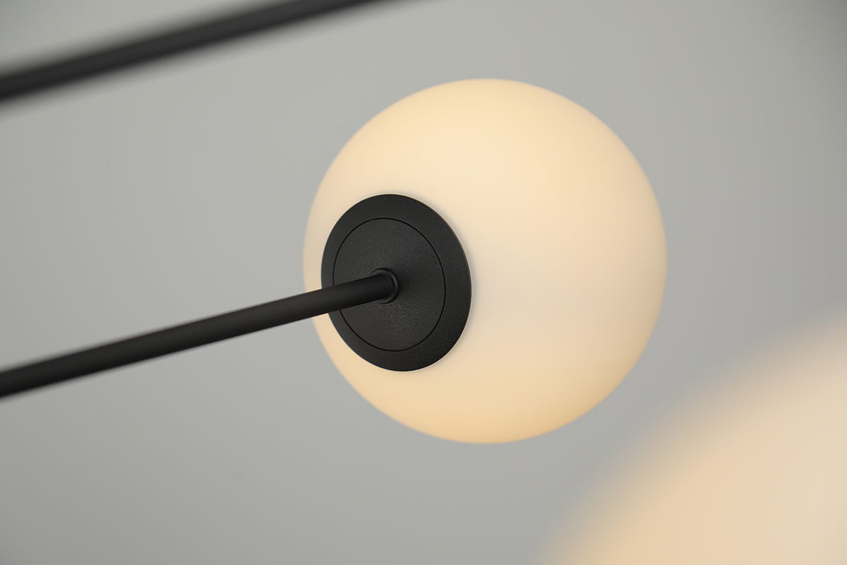Lampa wisząca Oviedo 8-punktowa w kolorze czarnym, z okrągłymi, mlecznymi kloszami. Widok zbliżeniowy na jedno z mocowań, z czarnym elementem montażowym i metalowym prętem. Prosta, nowoczesna forma, odpowiednia do różnych wnętrz.