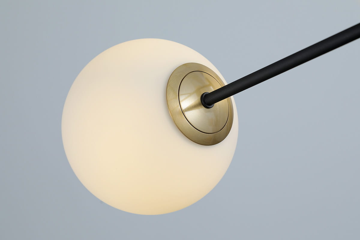 Lampa wisząca Oviedo 6-punktowa w kolorze czarnym i złotym. Szklana kula w białym odcieniu, zawieszona na cienkiej czarnej rurce, montowana do sufitu za pomocą złotego mocowania. Ujęcie z góry, ukazujące detale mocowania i teksturę szkła.