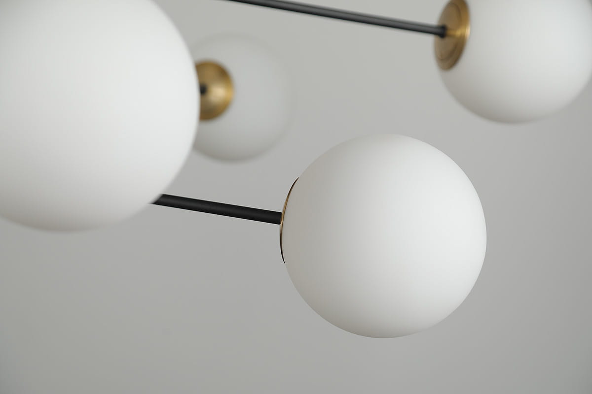 Lampa wisząca Oviedo 8-punktowa w kolorze czarnym i złotym. Składa się z białych, matowych kul o gładkiej powierzchni, zamocowanych na cienkich, czarnych ramionach. Ujęcie z góry, ukazujące detale wykończenia i połączenia z metalowymi elementami.