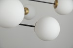 Lampa wisząca Oviedo 8-punktowa w kolorze czarnym i złotym. Składa się z białych, matowych kul o gładkiej powierzchni, zamocowanych na cienkich, czarnych ramionach. Ujęcie z góry, ukazujące detale wykończenia i połączenia z metalowymi elementami.
