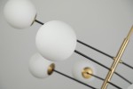 Lampa wisząca Oviedo 8-punktowa w kolorze czarnym i złotym, z białymi, matowymi kulami. Ujęcie z bliska pokazuje detale mocowania i struktury ramy. Elementy metalowe w złotym wykończeniu kontrastują z czarnymi prętami.
