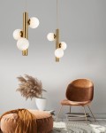 Złota lampa wisząca 3-punktowa Cortega z trzema białymi kulistymi kloszami, zawieszona w przestrzeni. Lampa ma minimalistyczny design i jest umiejscowiona nad stylowym, brązowym fotelem oraz okrągłym pufem na tle jasnej ściany.
